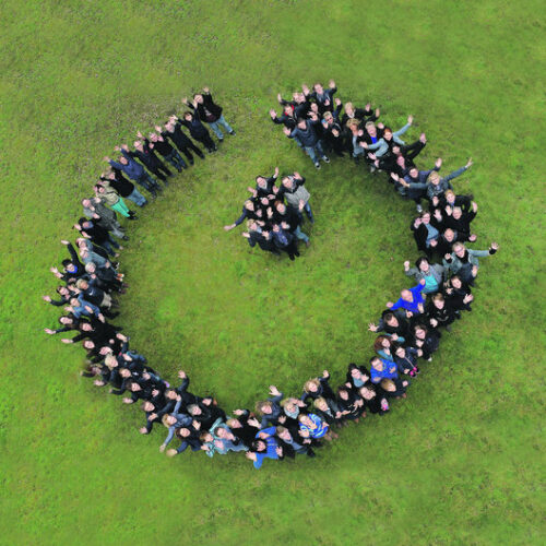 Aus der Luft fotografiert, formt eine Menschenmenge auf Rasen stehend das Logo der Lebenshilfe.